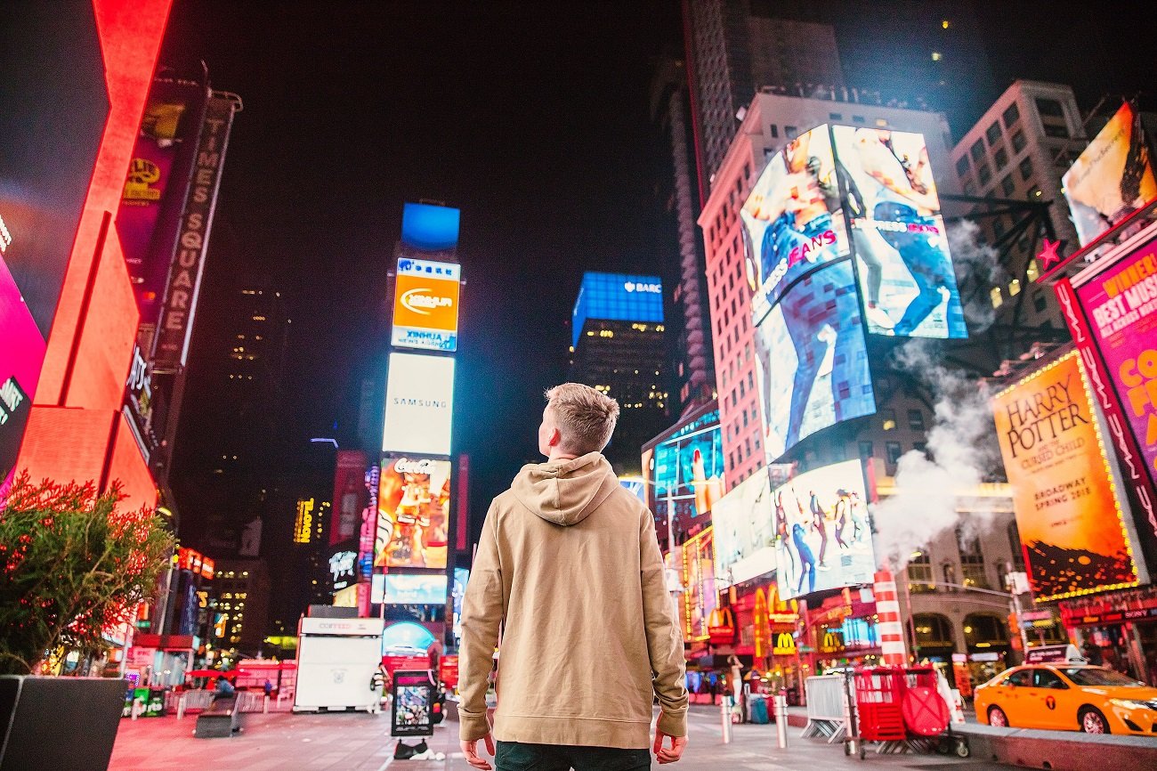 personne face à plusieurs bannières publicitaires sur Time Square, l'importance pour une entreprise de bien choisir ses supports de communication pour sortir du lot